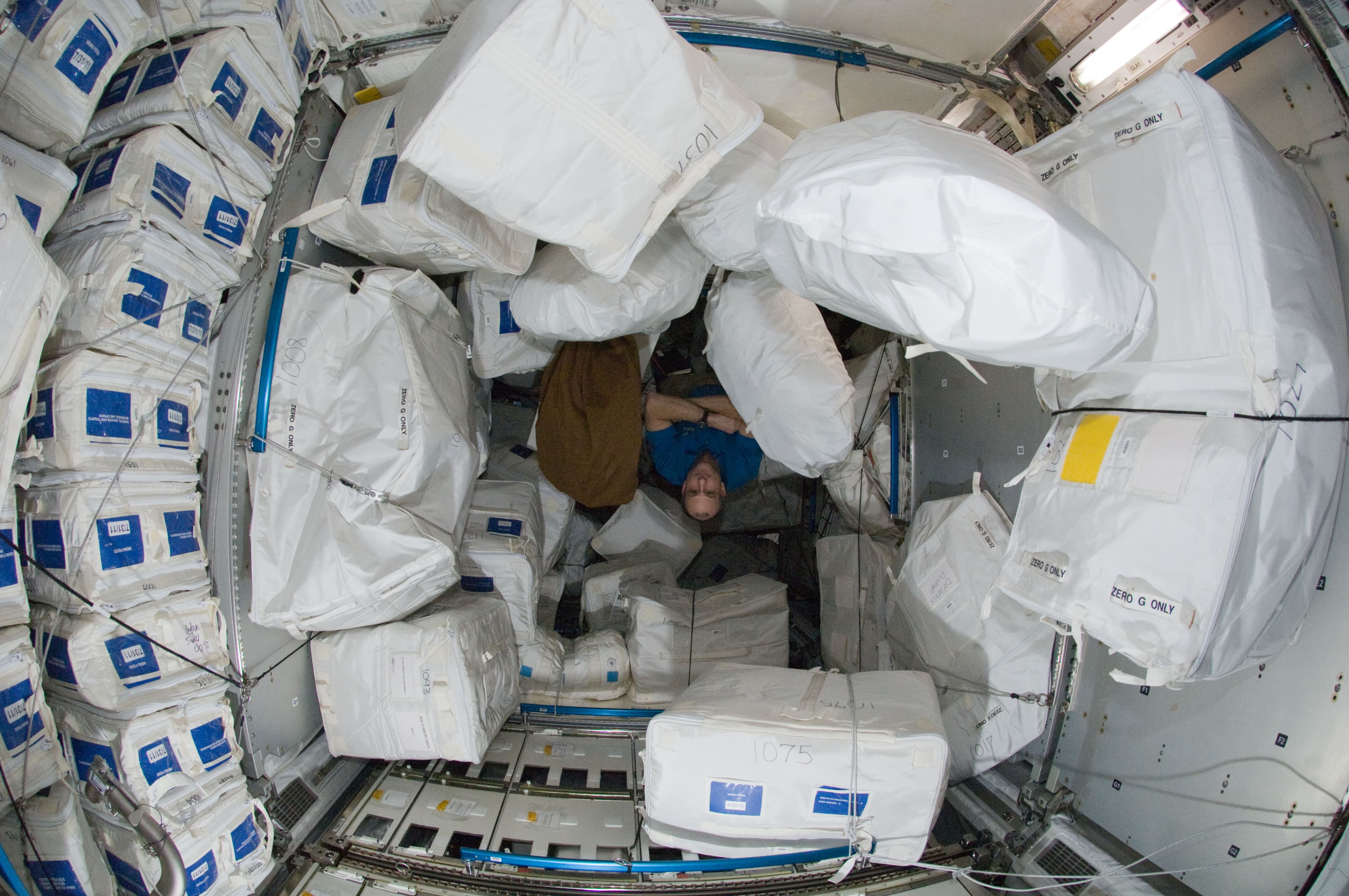 Astronaut surrounded by soft cargo bags and cluttered stowage inside the ISS